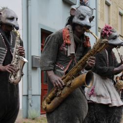 3 Personen in Rattenkostümen spielen Trompete, Saxophon und Flöte.