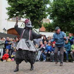 Frau in Rattenkostüm tanzt über den Marienplatz und dahinterstehender Mann hält spielerisch den Rattenschwanz hoch.